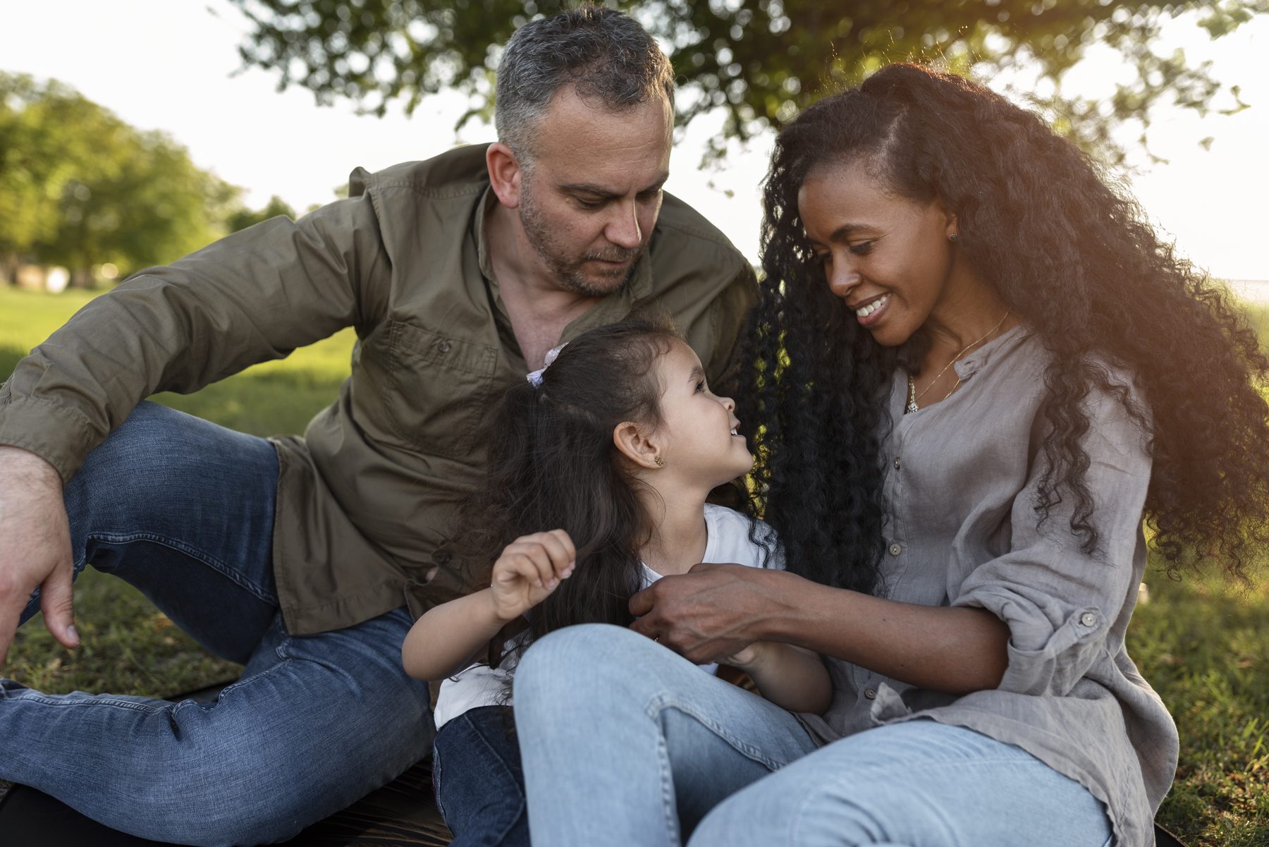 Una madre y un padre juegan con su hija en un parque, al final de la tarde